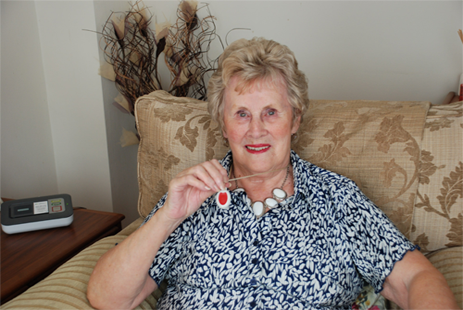 Joan, a Lifeline alarm user, holding up her MyAmie pendant