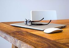 Glasses on top of laptop and mouse on wooden desk